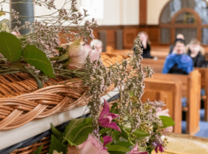 A small funeral congregation in a UK church with a wicker coffin in the foreground